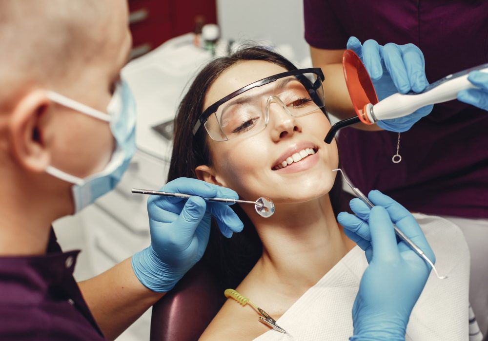 The dentist treats the girl's teeth. A young woman visited a dentist. The doctor works with an assistant
